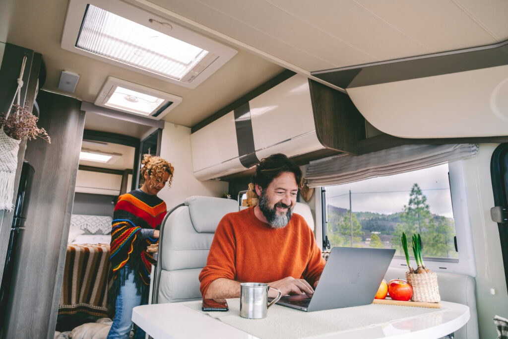 A couple wearing colorful clothes inside of their camper van using a camping reservation software in his laptop