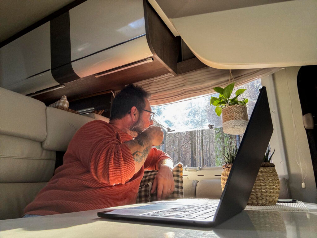 A man using his laptop inside of a camper van while drinking coffee 