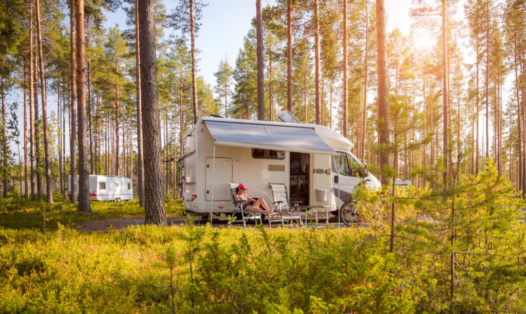 a person enjoying a stay in front of a camper van in the forest of a RV park spot