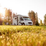 a low pov of a camper van in the forest with the sun on the left