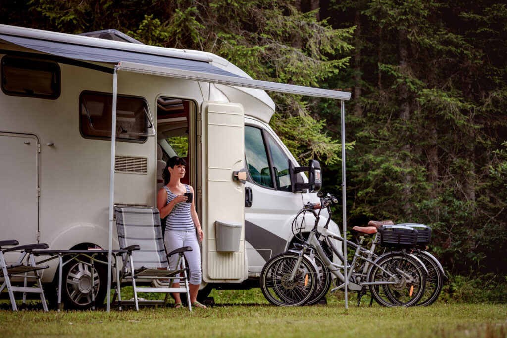 a woman drinking coffee outside of her camper van in a RV park 