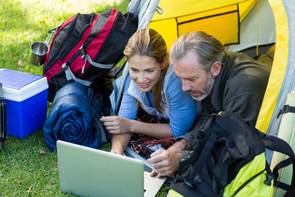 Two people checking campground software reservation marketplace on a laptop inside a camping tent 