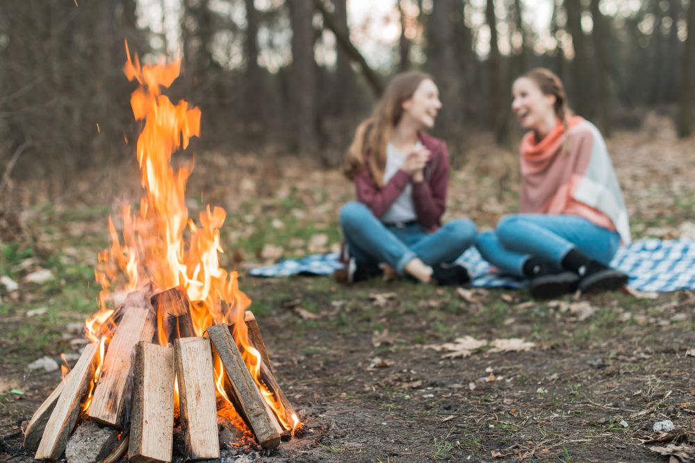 two women enjoying a day camping in the fall in front of a campfire 