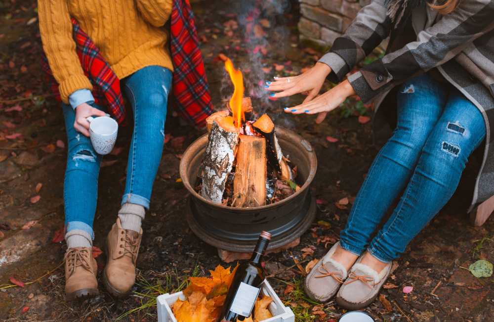 two people warming their hands in front of a campfire during fall