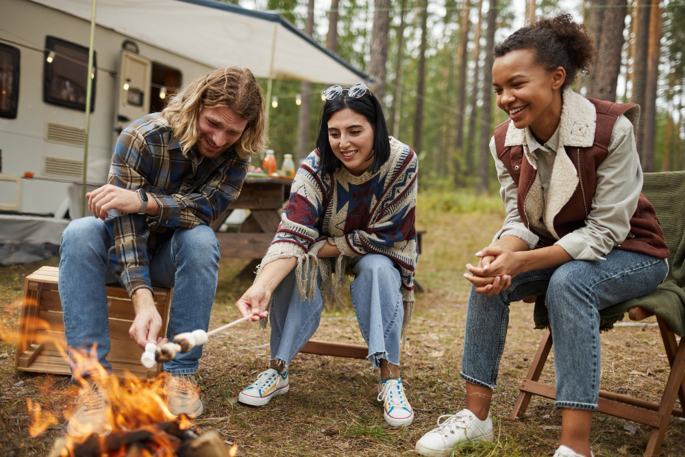 Three friends in front of a campfire cooking marshmellows thanks to multiple booking sites 