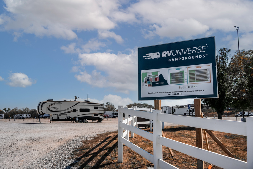 Campground sign, entrance and camper parked on gravel campsite